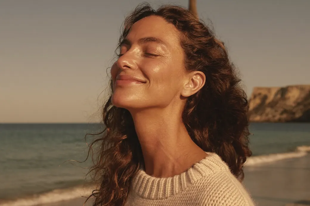 Woman with sun-kissed skin, eyes closed, smiling in the warm evening sun on a beach
